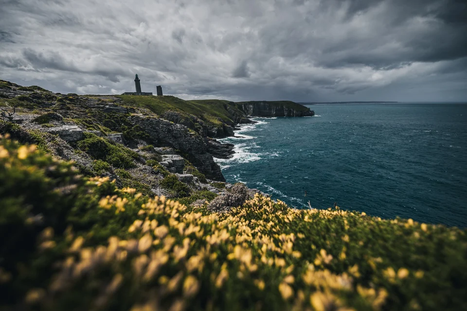 Côte rocheuse de Bretagne, fleurs jaunes et tours au loin sous les nuages