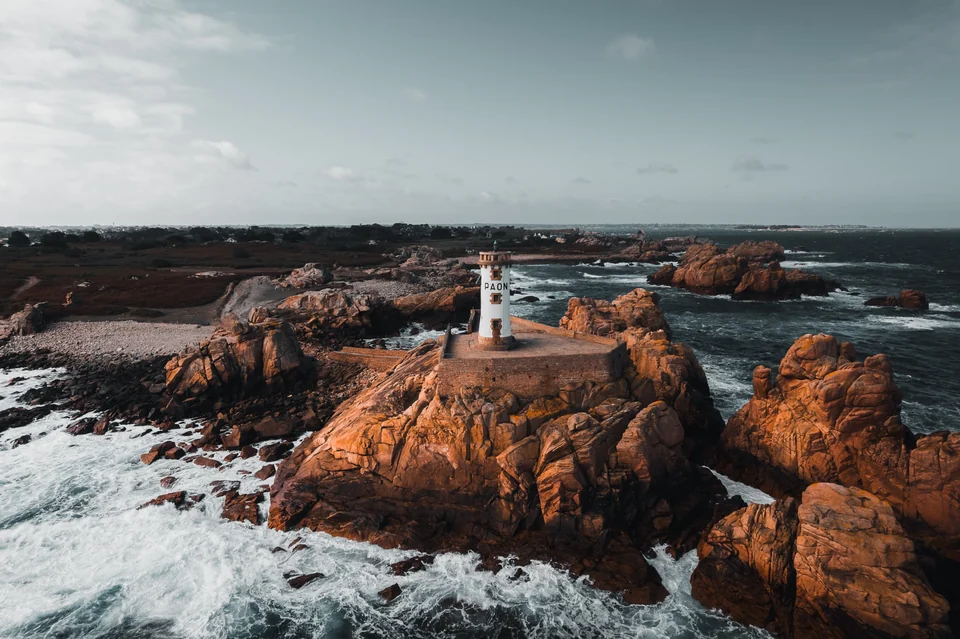 Phare entouré de rochers de granit rose et d’écume en Bretagne, vu du ciel