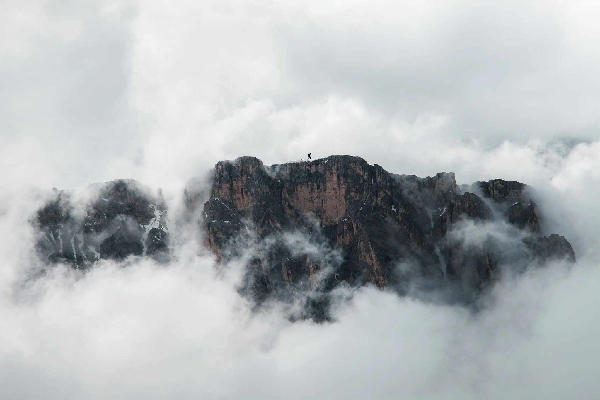 Crête rocheuse émergeant des nuages, avec une silhouette au sommet