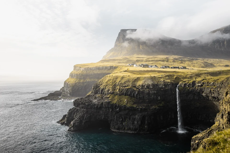 Cascade de Múlafossur sous une éclaircie, entre falaises, brume et océan aux îles Féroé
