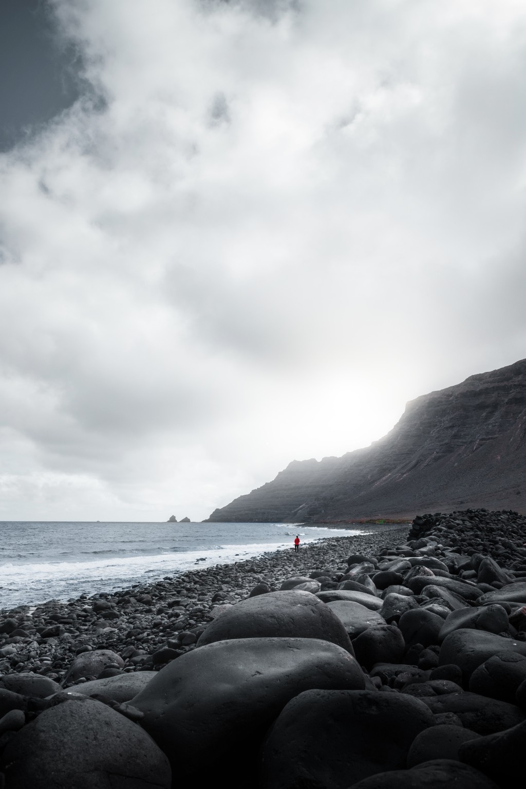 Silhouette en rouge sur une plage de galets noirs au pied des falaises de Lanzarote
