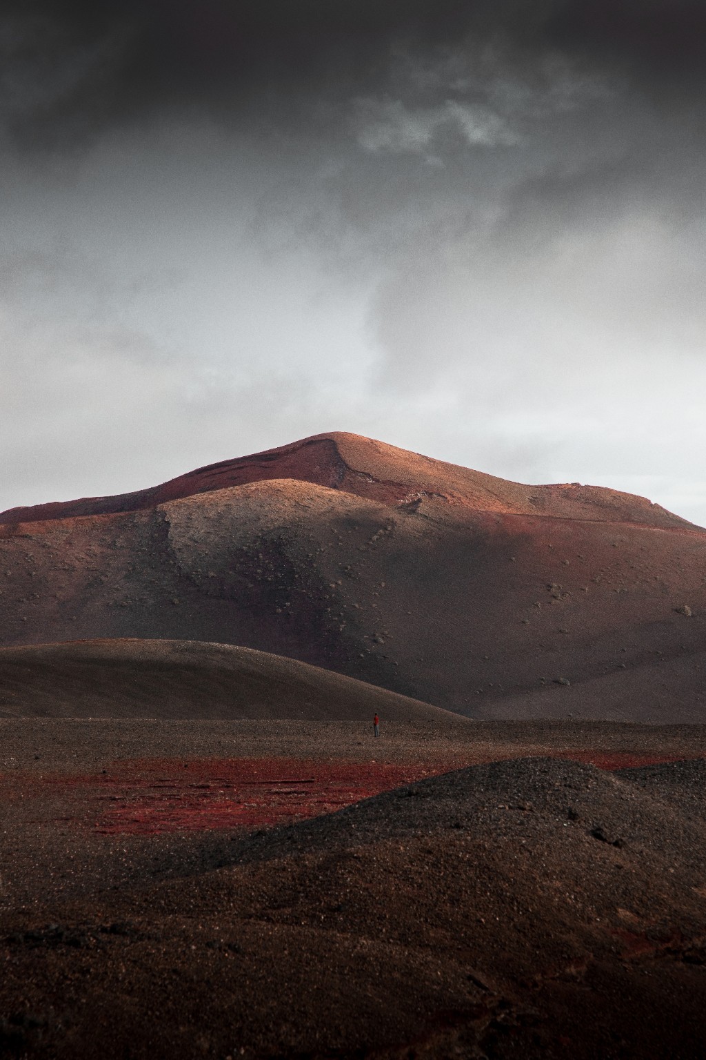 Silhouette en rouge au pied d’un relief volcanique ocre et noir à Lanzarote