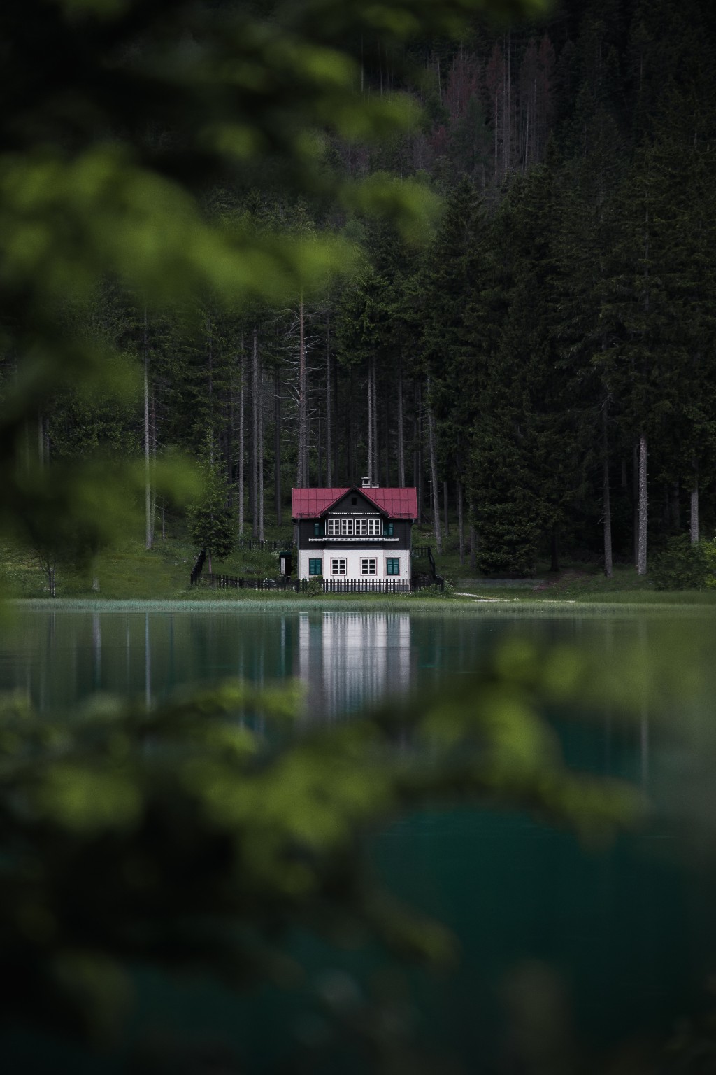 Maison au toit rouge se reflétant dans un lac devant une forêt sombre