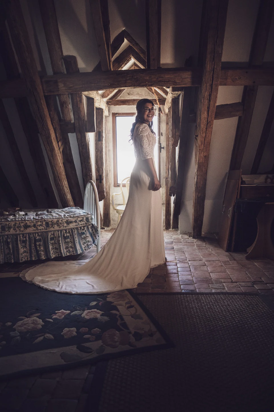 La mariée dans sa robe blanche dans une chambre aux poutres apparentes