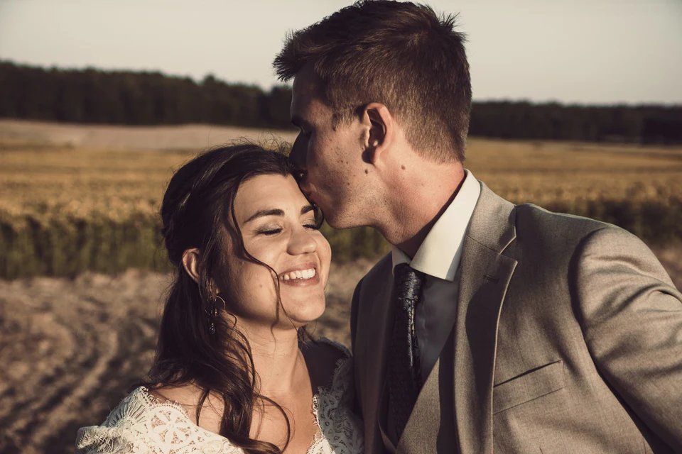 Le marié embrasse la mariée sur le front dans un champ