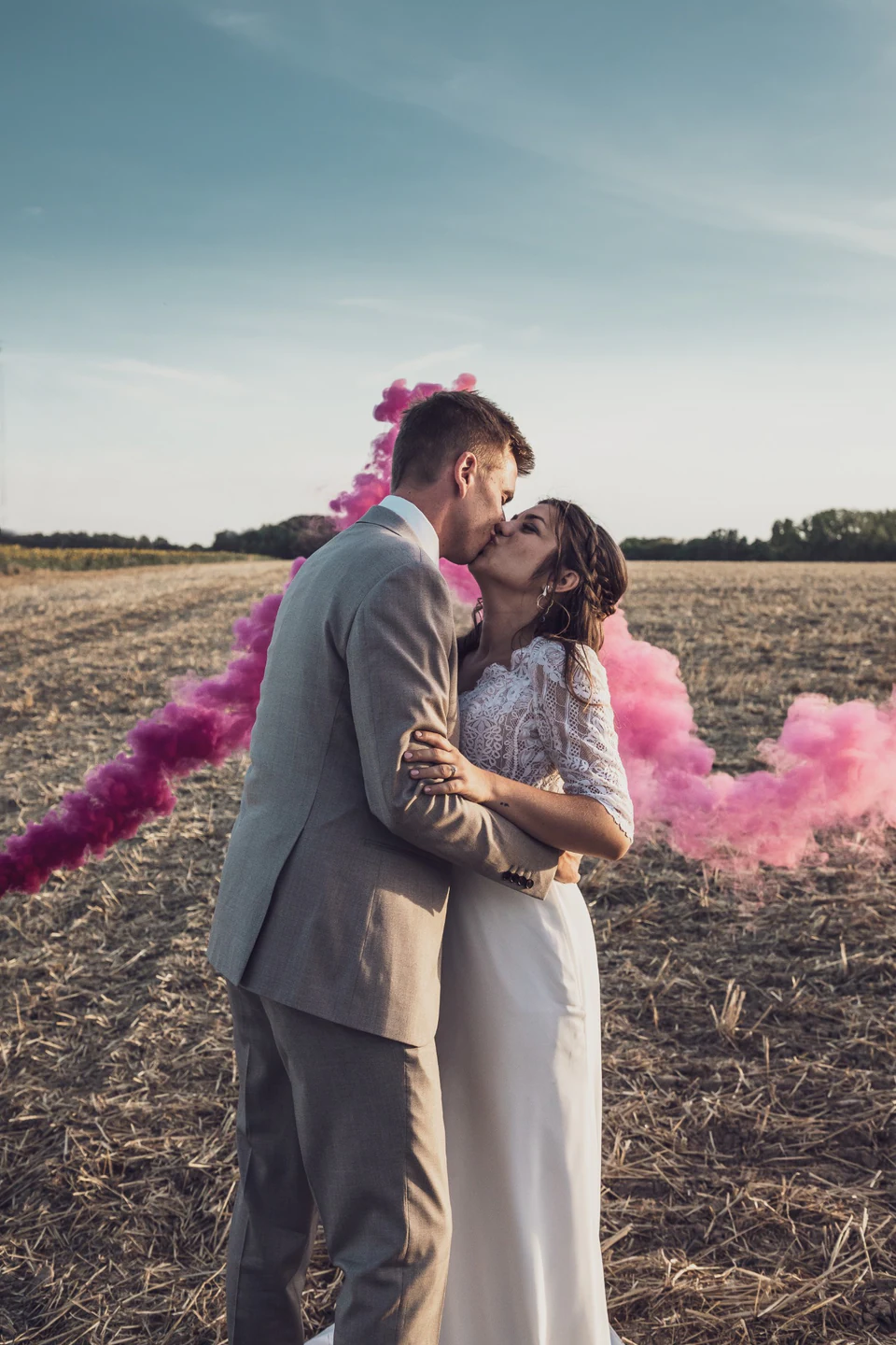 Les mariés s'embrassent devant une fumée rose dans un champ